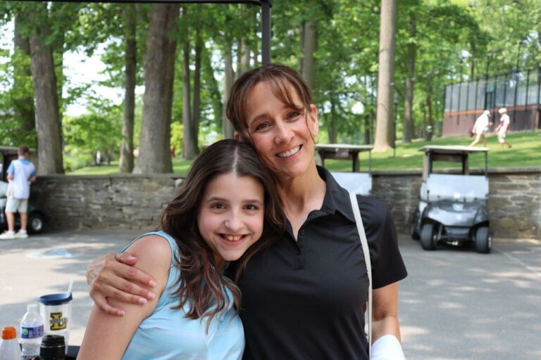 A woman and a young girl stand side by side, smiling at the camera